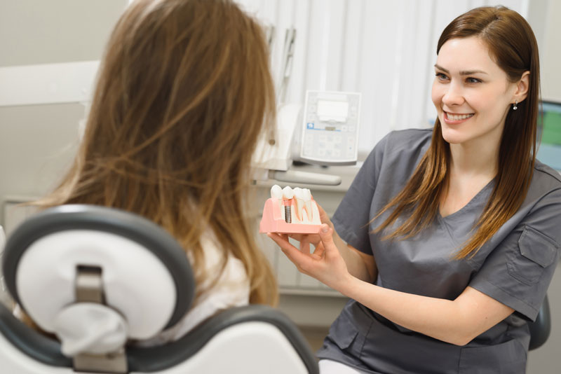 a doctor showing a patient a dental implant model so she can learn how dental implants can improve the functionality of her teeth.