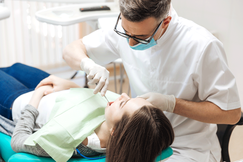 Professional dentist doing teeth checkup on female patient dental surgery.